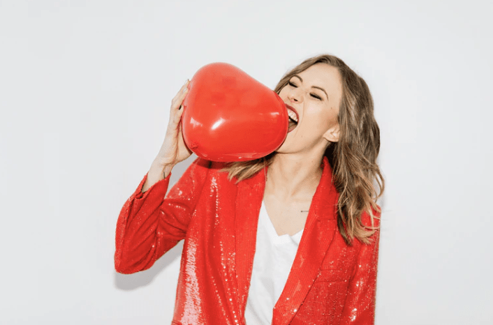 Oppas met rood jasje aan. Rode hartjes ballon in haar hand waar ze in bijt