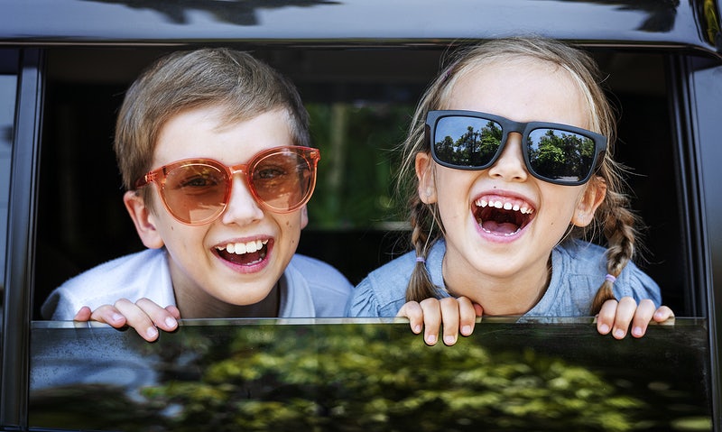 Jongen en een meisje die samen uit het raam van een auto hangen. Lachen allebei en hebben een zonnebril op